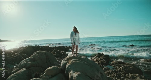 Woman standing on rocks at the beach while waves crash in slow motion