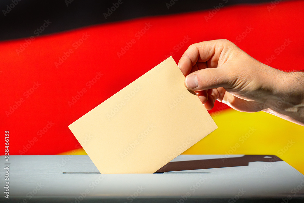 Voting envelope is thrown into ballot box. Beige envelope in hand. Flag of Germany in the background. Election year 2024 in Germany. Voting envelope is thrown into ballot box. Beige envelope in hand. Flag of Germany in the background. Election year 2024 in Germany.