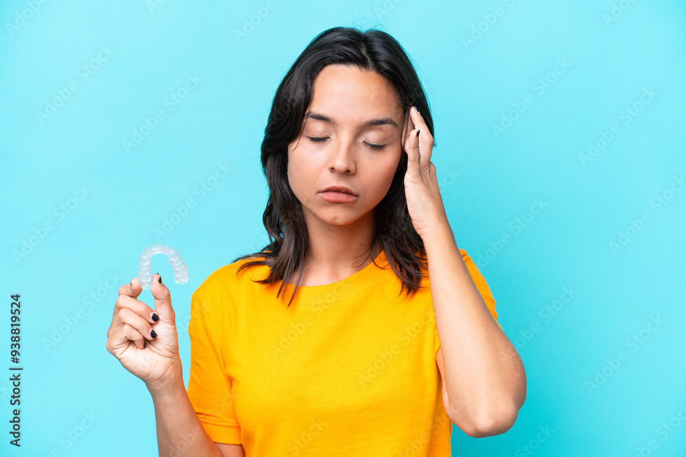 Young hispanic woman holding invisible braces isolated on blue background with headache Young hispanic woman holding invisible braces isolated on blue background with headache