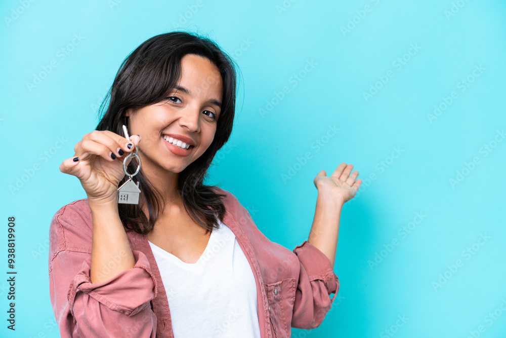 Young hispanic woman holding home keys isolated on blue background extending hands to the side for inviting to come Young hispanic woman holding home keys isolated on blue background extending hands to the side for inviting to come