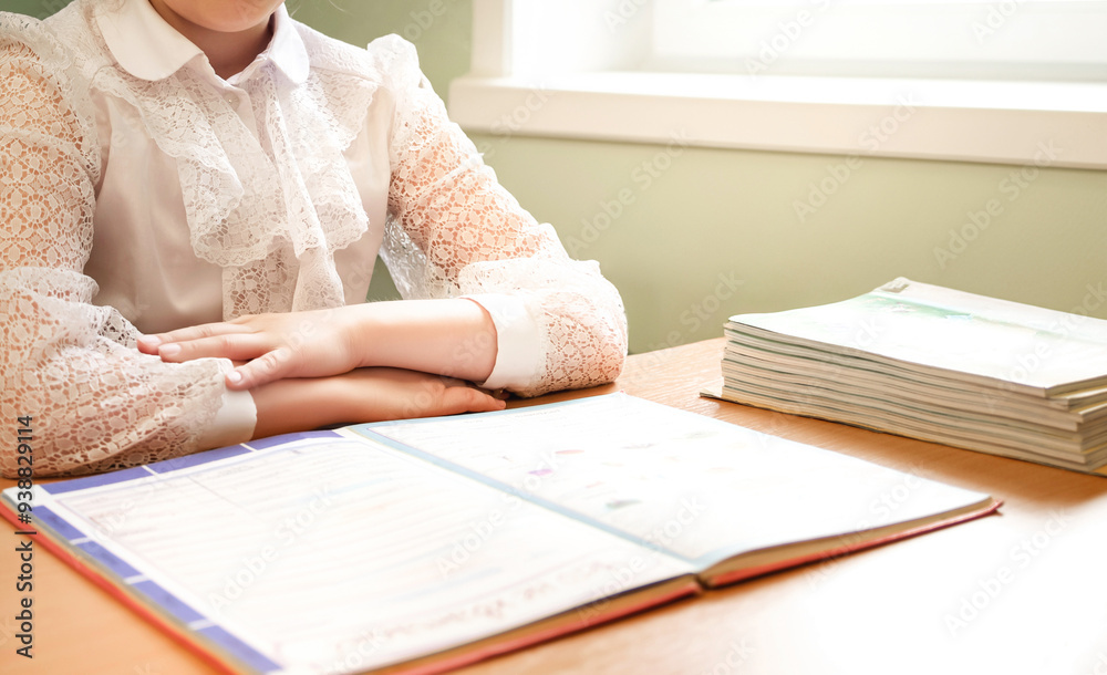 A schoolgirl is sitting at her desk in the first lesson at school. A stack of textbooks. Back to school