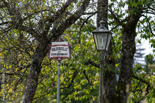 Uraltes Strassenbahnhaltestellenschild neben einer alten Laterne unter Apfelbäumen, Nostalgie photo