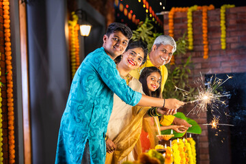 Indian young family with kids celebrating Diwali festival with sparklers in gallery