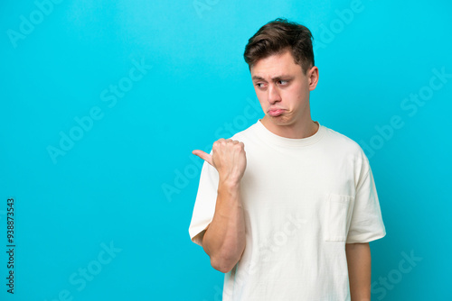 Young handsome Brazilian man isolated on blue background unhappy and pointing to the side