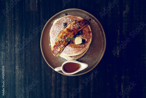 Banana pancakes breaksfast with Mapple syrup on a ceramic plate with a caramelized banana as a decoration on a black wooden table photo