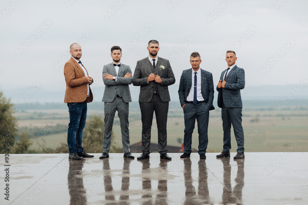 A group of five men are standing on a wet surface, dressed in suits and ...
