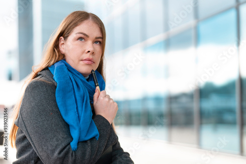 Young Woman Student in Blue Scarf Contemplating Outdoors Near Modern Building on a Sunny Day photo