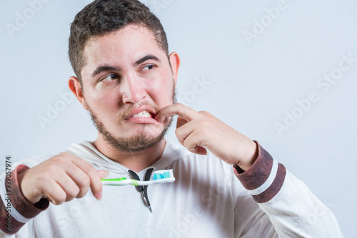 Young man with tooth sensitivity holding a toothbrush isolated. Man suffering from gum pain holding brush photo