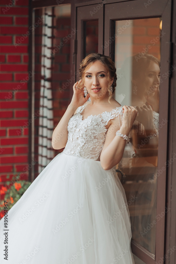 A woman in a white dress is standing in front of a brick building. She is wearing a necklace and earrings A woman in a white dress is standing in front of a brick building. She is wearing a necklace and earrings