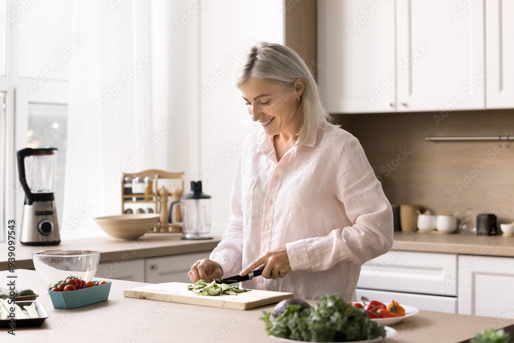 Happy mature woman spends weekend time in kitchen, cut fresh vegetables for vegetarian salad, try new dietary recipe, lead healthy lifestyle, enjoy culinary hobby, prepare delicious dinner for family Happy mature woman spends weekend time in kitchen, cut fresh vegetables for vegetarian salad, try new dietary recipe, lead healthy lifestyle, enjoy culinary hobby, prepare delicious dinner for family