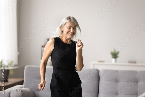 Lively middle-aged female listens favourite music and dancing in modern living room alone on weekend leisure, celebrate great news, relish life looking carefree and contented. Hobby, active lifestyle photo