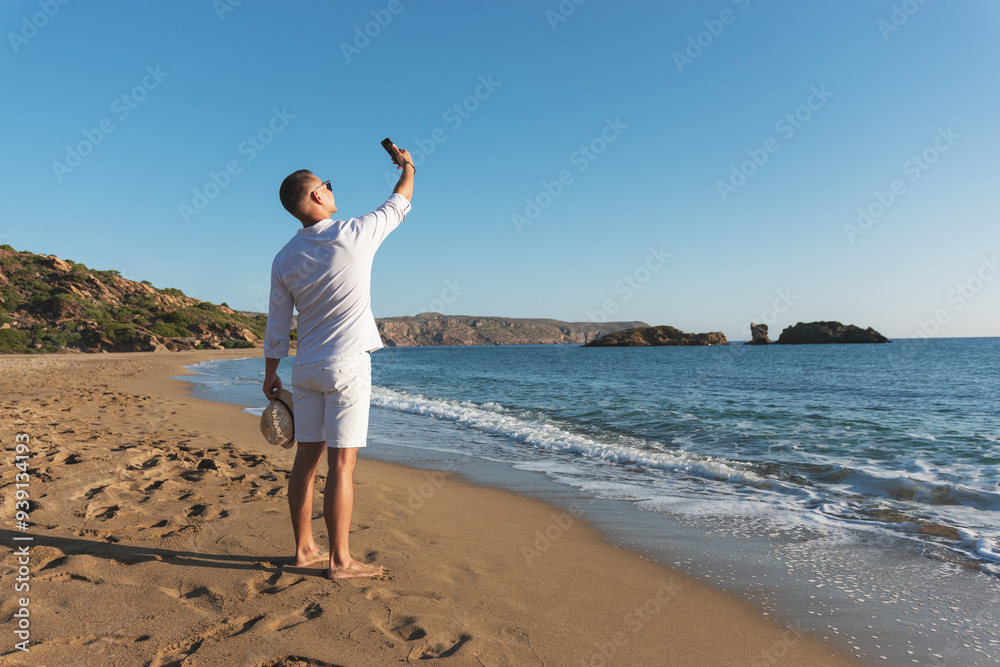 Handsome happy man in white shirt taking selfie on the beach. Summer vacations concept. Handsome happy man in white shirt taking selfie on the beach. Summer vacations concept.