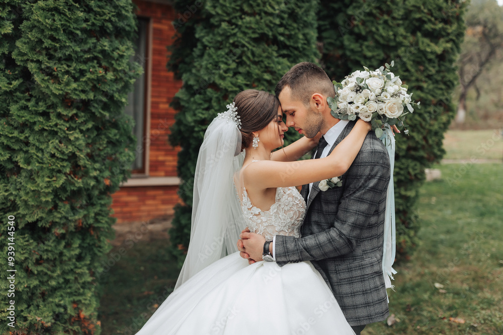 A bride and groom are embracing each other in front of a building. The bride is wearing a white dress and the groom is wearing a suit. They are holding hands and smiling at the camera A bride and groom are embracing each other in front of a building. The bride is wearing a white dress and the groom is wearing a suit. They are holding hands and smiling at the camera