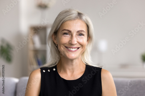 Fototapeta Naklejka Na Ścianę i Meble -  Head shot portrait pretty blonde woman looking at camera, sits alone on sofa photoshooting, enjoy pleasant pastime weekend at home at own or rented apartment. Beautiful mature female profile picture