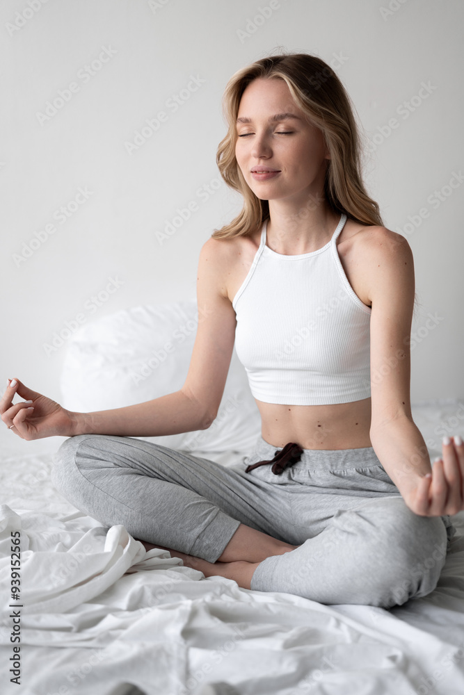young woman wearing top practicing meditation on the bed at home. young woman wearing top practicing meditation on the bed at home.