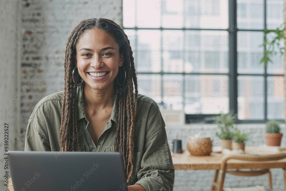Happy young woman student with dreadlocks is sitting at a table with a laptop in front of her, she is smiling and looking on camera with copy space Happy young woman student with dreadlocks is sitting at a table with a laptop in front of her, she is smiling and looking on camera with copy space