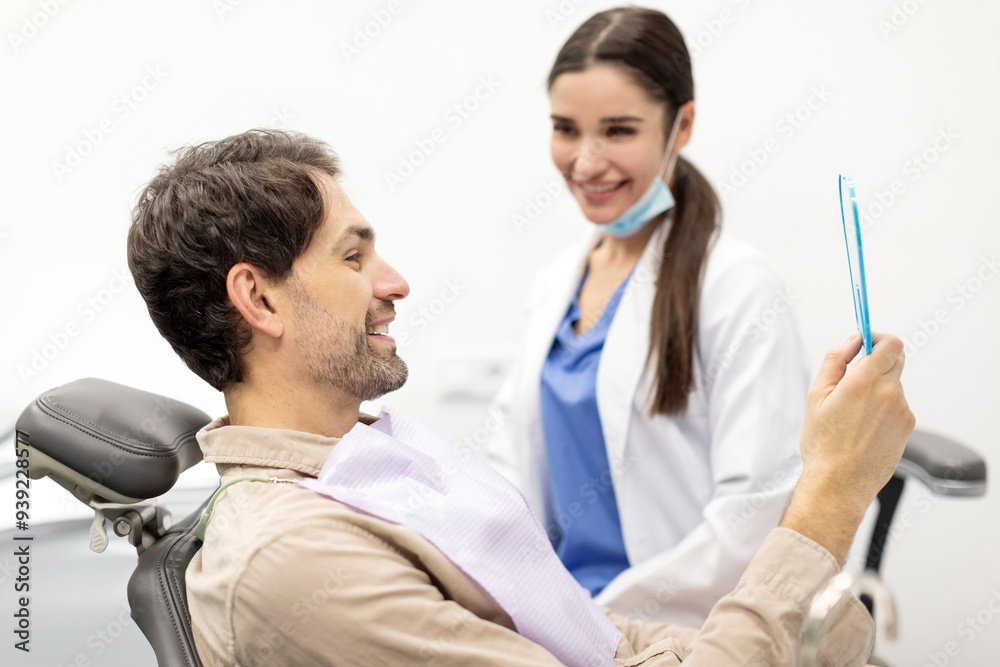 Happy male patient looking in the mirror and checking teeth after professional dental treatment in clinic Happy male patient looking in the mirror and checking teeth after professional dental treatment in clinic