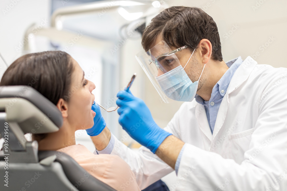 Professional male dentist orthodontist in protective face mask curing operating woman teeth, healing caries decay Professional male dentist orthodontist in protective face mask curing operating woman teeth, healing caries decay