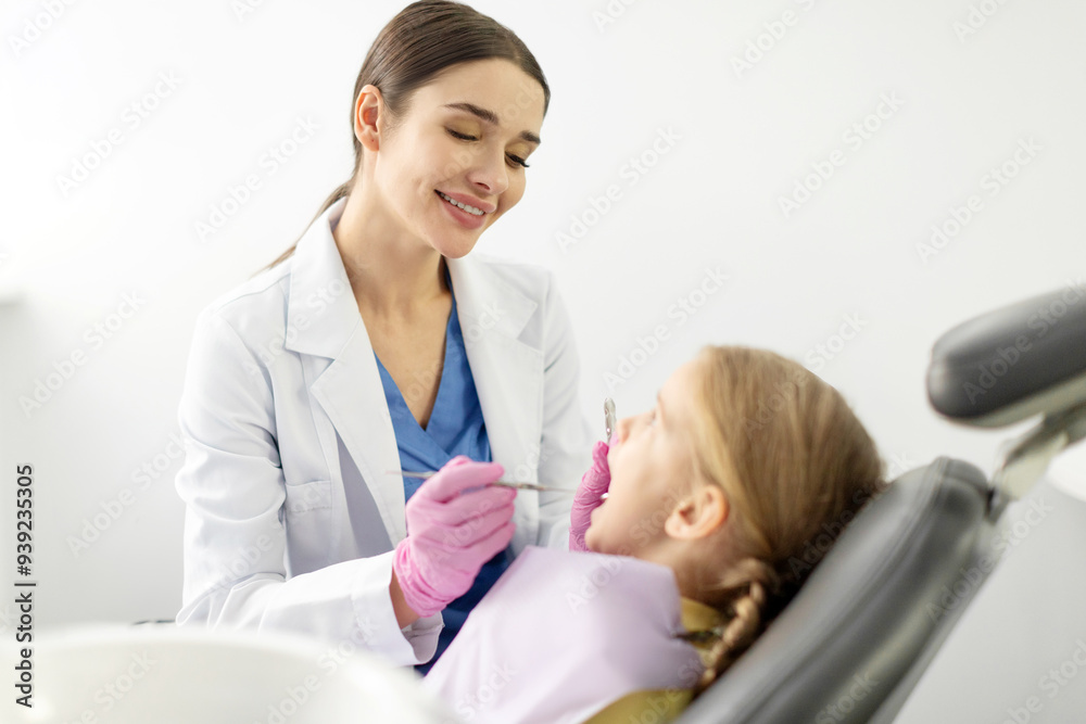 Young woman dentist treating kid tooth, little girl sitting in dentists office. Dentist examining female child patient's teeth Young woman dentist treating kid tooth, little girl sitting in dentists office. Dentist examining female child patient's teeth