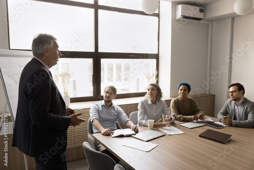 Mature businessman in suit hold formal meeting with stakeholders met in modern boardroom, introduce new corporate goals or project details, share opinion, strategy and plan, leading briefing for staff photo