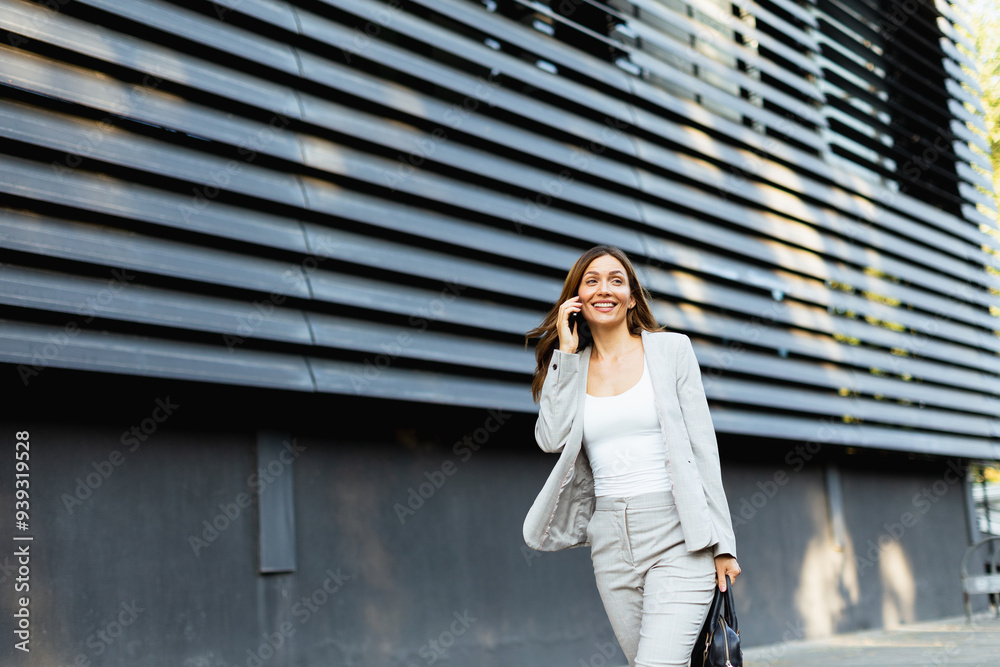 Confident business woman enjoying a sunny day while walking outdoors and chatting on the phone near a modern building Confident business woman enjoying a sunny day while walking outdoors and chatting on the phone near a modern building