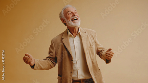 A cheerful elderly man dances joyfully against a beige studio backdrop, capturing happiness and vitality in senior years with a warm, engaging smile.