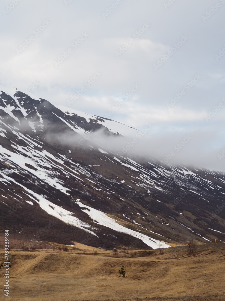 A majestic mountain partly covered in snow is shrouded in misty clouds ...