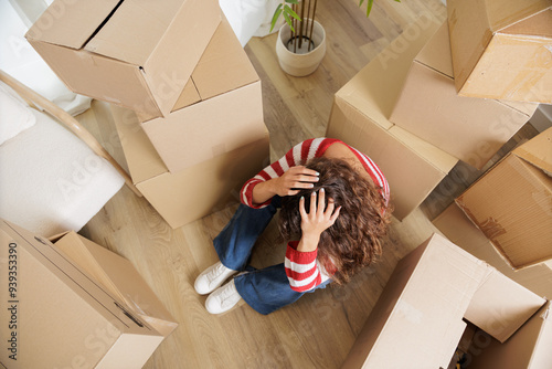 Slika na platnu Young woman overwhelmed in her new house surrounded by cardboard boxes that reach the ceiling