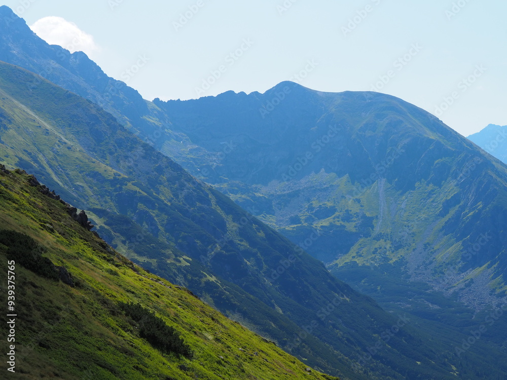 An expansive view of a mountain range with rocky peaks and lush greenery under a clear sky, showcasing the grandeur and unspoiled beauty of the natural environment. An expansive view of a mountain range with rocky peaks and lush greenery under a clear sky, showcasing the grandeur and unspoiled beauty of the natural environment.