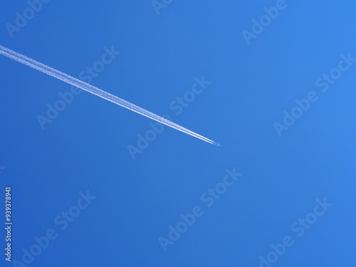 An airplane flies high in the clear blue sky, leaving behind distinct contrails as it moves, depicting freedom and travel, and capturing a moment of serene sky beauty