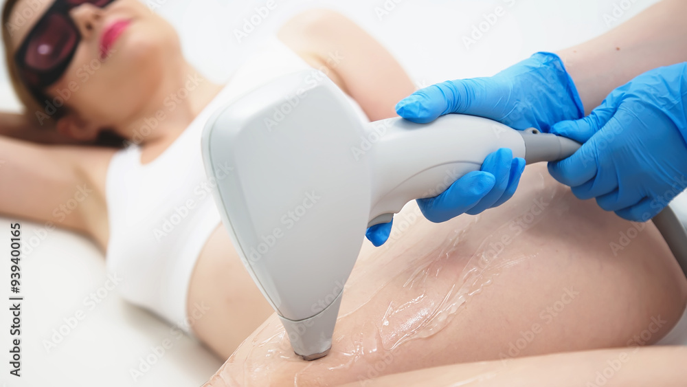 Naklejka premium A female cosmetologist performs laser hair removal on a young woman's smooth legs in a modern beauty salon. Close-up of body care and spa treatments, showcasing professional aesthetics.