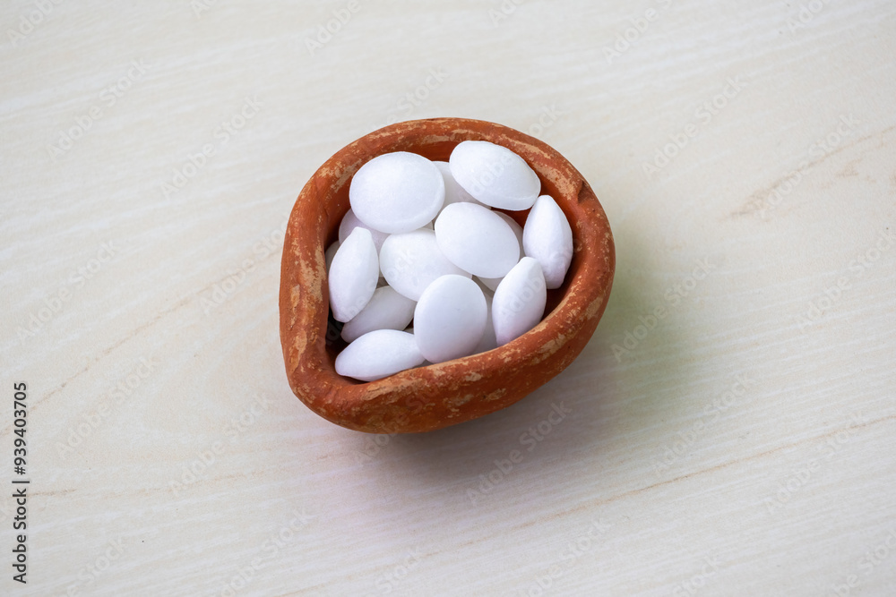 An earthen pot full of white naphthalene balls on wooden background. It is also known as moth balls, naphthalin, moth flakes, antimite, and hexalene. An earthen pot full of white naphthalene balls on wooden background. It is also known as moth balls, naphthalin, moth flakes, antimite, and hexalene.