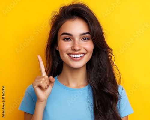 Smiling Woman with Long Hair Points Up Against Yellow Background Portrait Composition Happy Expression Focused Finger 179 characters