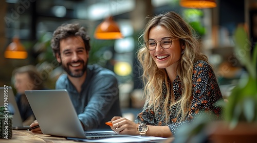 A cheerful business team gathered around a project, laptops in use, sharing laughs in a modern office