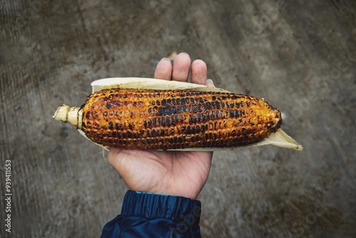 Spicy, salted roasted corn holding in hand outdoors in rainy season