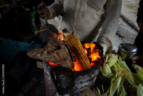 Seller man making roasted grilled corn in streets in rainy season, India