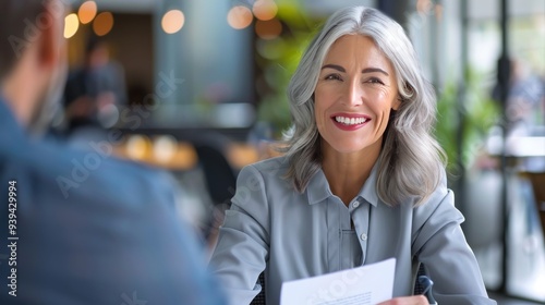 Fototapeta Naklejka Na Ścianę i Meble -  Smiling mature business woman hr holding cv document at job interview. Happy mid aged professional banking manager or lawyer consulting client sitting at workplace in corporate office meeting.