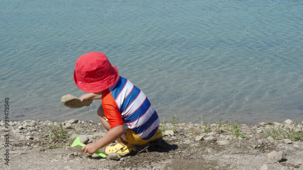 Small child wearing sun protection shirt playing on the lake shore on a summer day.