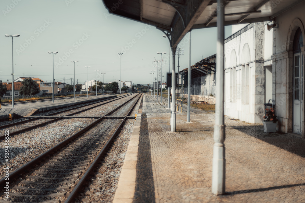 An empty, quiet railway station with multiple tracks leading into the distance. The platform is lined with lampposts and an old building, capturing a peaceful, nostalgic scene An empty, quiet railway station with multiple tracks leading into the distance. The platform is lined with lampposts and an old building, capturing a peaceful, nostalgic scene