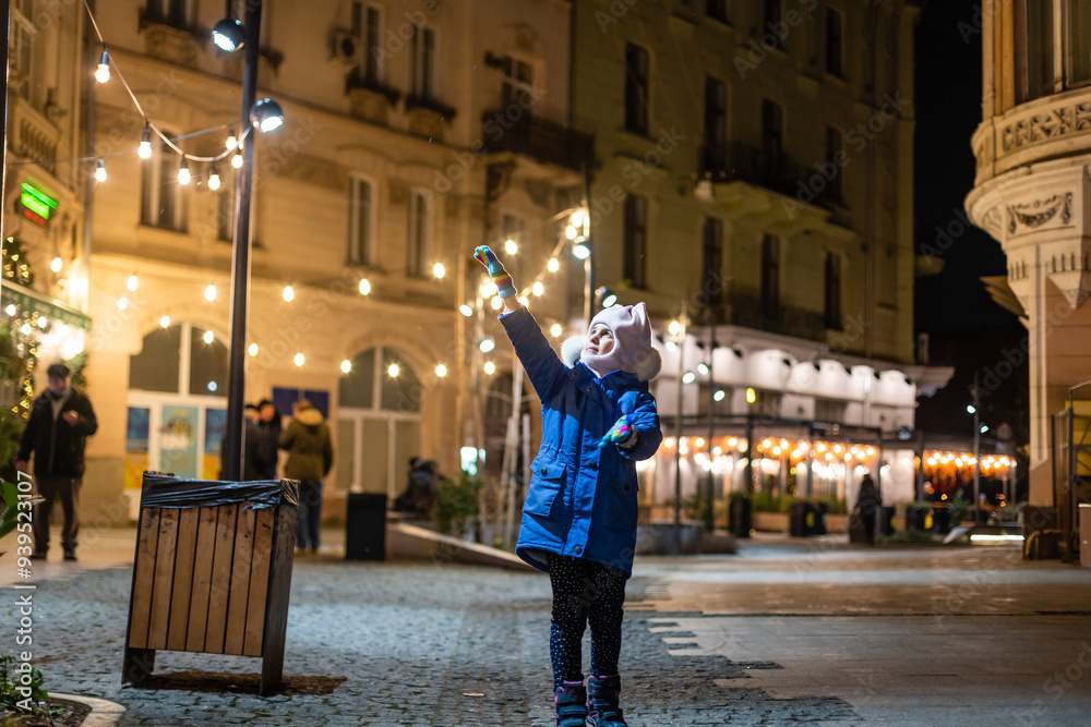 Obraz premium Little girl, iluminated with street lights. Christmas decoration is in the background