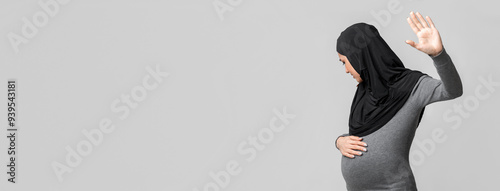 Islam And Domestic Violence Concept. Scared pregnant muslim woman in hijab doing stop gesture, hiding face and touching her belly on grey background photo