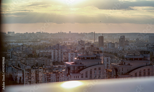 The sun sets over Kyiv, casting a soft golden light over the sprawling cityscape. High-rise buildings catch the last rays of the day, creating a tranquil and picturesque urban scene.