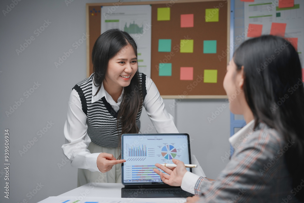 Two businesswomen are smiling while analyzing positive financial data on a tablet during a business meeting Two businesswomen are smiling while analyzing positive financial data on a tablet during a business meeting