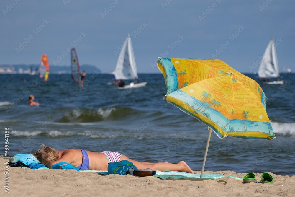 A woman in beachwear lies on the sand and sunbathes on the beach next to a sun umbrella. A woman in beachwear lies on the sand and sunbathes on the beach next to a sun umbrella.