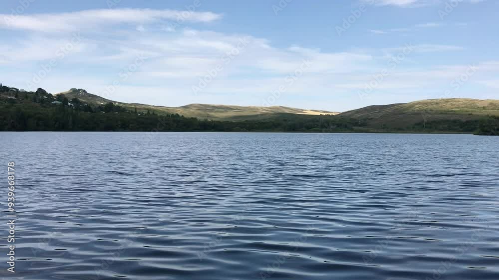 Tranquil Mountain Lake with Rippling Water Surface under a Clear Blue Sky on a Peaceful Summer Day in the Countryside with Rolling Hills in the Background Tranquil Mountain Lake with Rippling Water Surface under a Clear Blue Sky on a Peaceful Summer Day in the Countryside with Rolling Hills in the Background