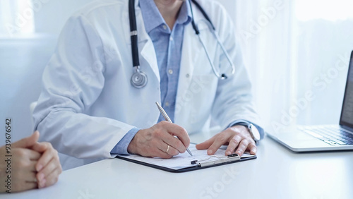 A doctor and a patient. The physician, wearing a white medical coat over a blue shirt, is filling out a medical record form during a consultation in the clinic. Medical service