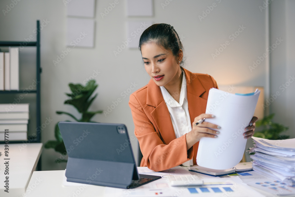 Businesswoman reading financial documents and working with tablet computer at office desk Businesswoman reading financial documents and working with tablet computer at office desk