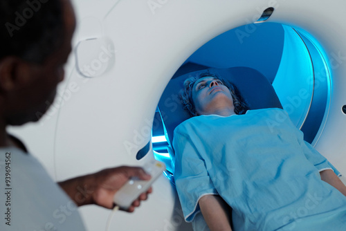 Person lying inside MRI scanner receiving diagnostic imaging with medical personnel operating machine nearby