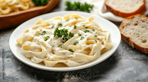 Fettuccine noodles in Alfredo sauce on a white plate with a slice of bread