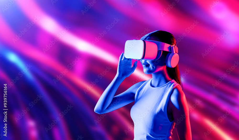 Smart female standing surrounded by neon light wearing VR headset connecting metaverse, future cyberspace community technology. Elegant woman looking faraway and smiling satisfactorily. Hallucination. Smart female standing surrounded by neon light wearing VR headset connecting metaverse, future cyberspace community technology. Elegant woman looking faraway and smiling satisfactorily. Hallucination.
